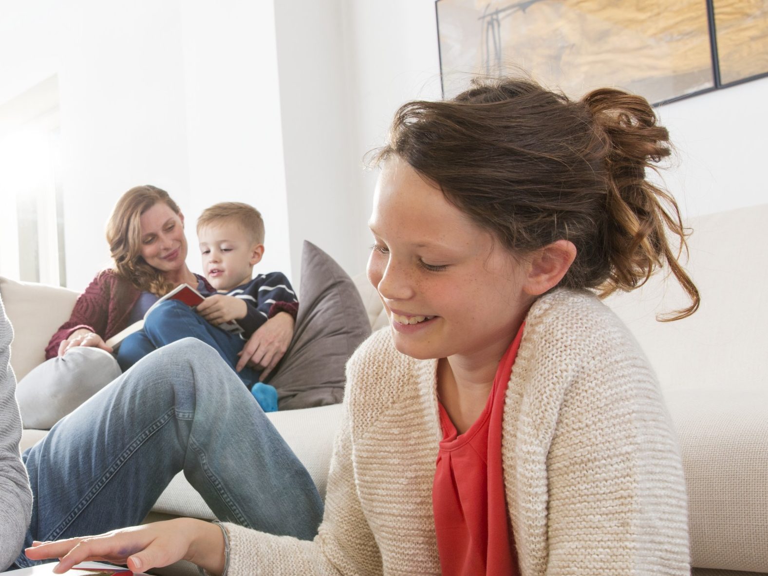 V popředí spokojená dívka usmívající v pozadí žena s dítětem čtoucí knihu | Zdravý domov