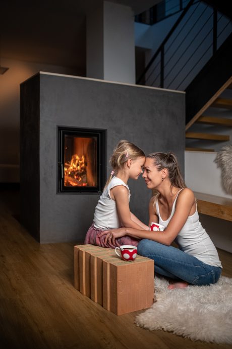 Žena maminka sedící s dítětem u teplého krbu v popředí cihla Porotherm T Profi